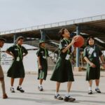 Group of children having fun playing basketball outdoors in school uniforms during the day.
