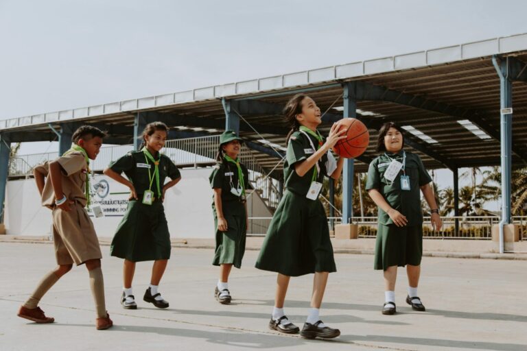 Group of children having fun playing basketball outdoors in school uniforms during the day.