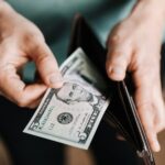 A person taking a five dollar bill from a wallet symbolizing personal finance and budget management.