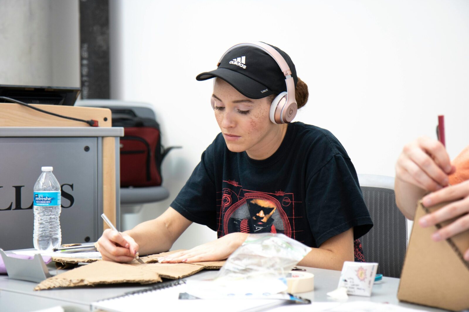 Young woman in headphones crafting at a table with cardboard for a school project, indoors.