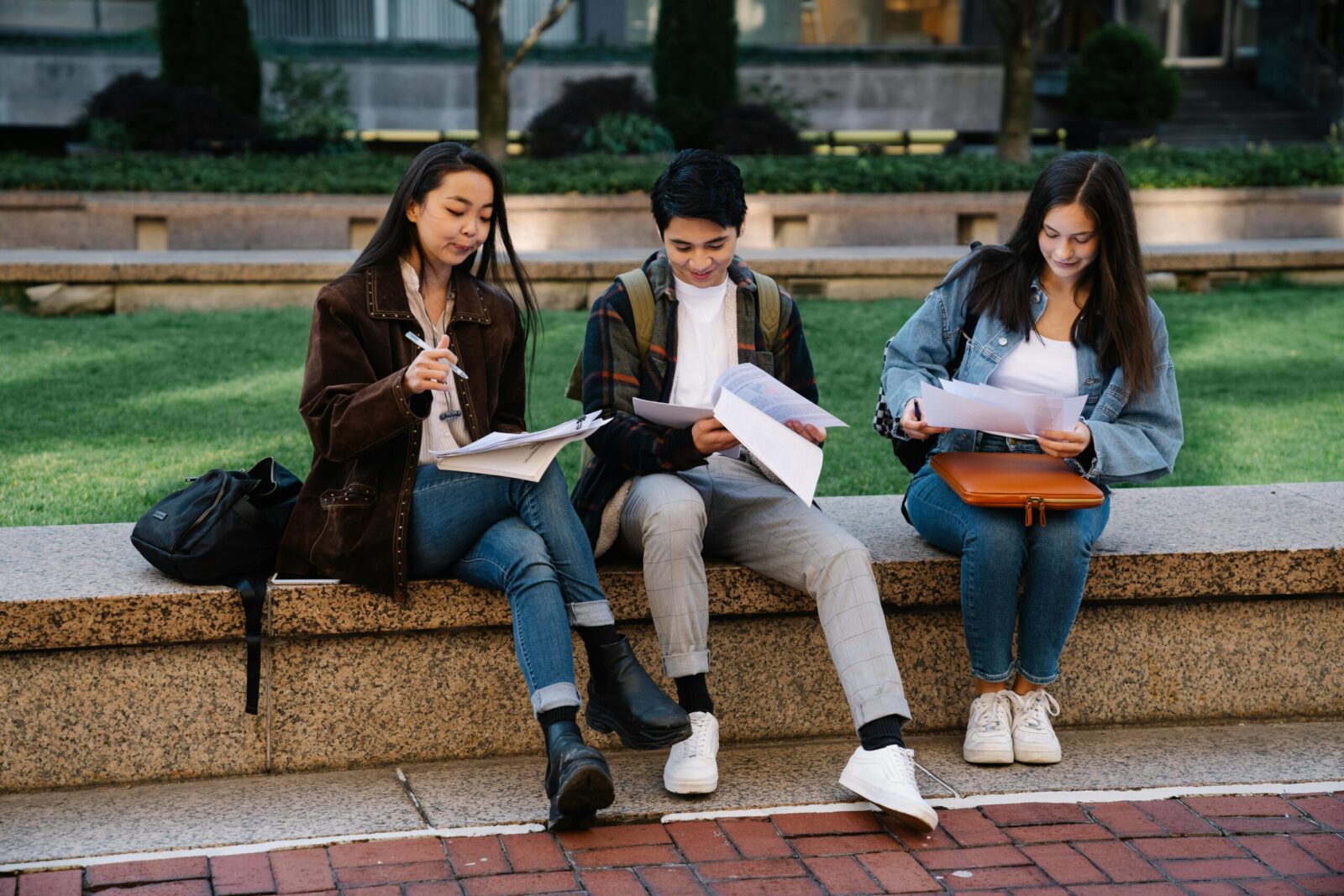 Three students studying together on a bench in a university campus setting outdoors.